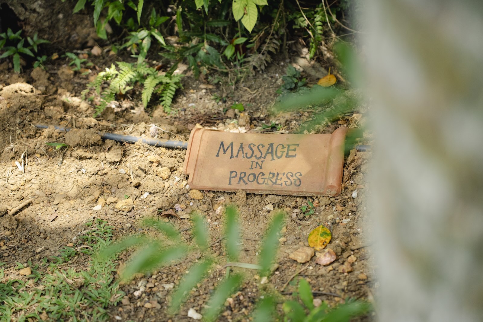 A hand-painted terracotta tile on the garden path reading “Massage in progress”